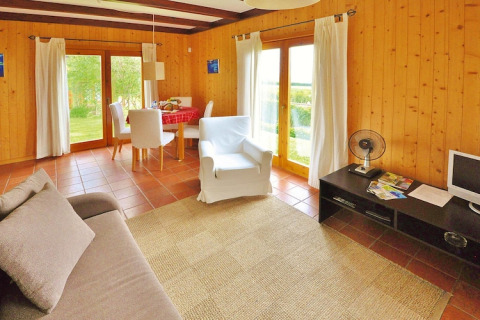 Houten woonkamer in bungalow met grote ramen, eethoek, bank, fauteuil en tv in Portugal.