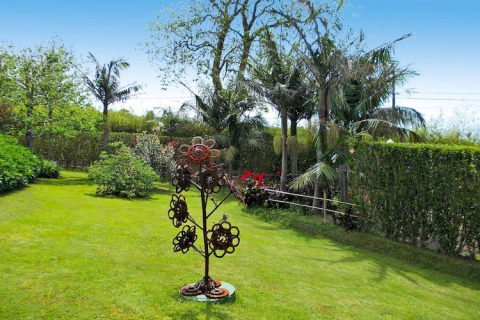 Groene tuin met palmbomen, struiken en een metalen bloemsculptuur bij Quinta dos Curubás in Portugal.