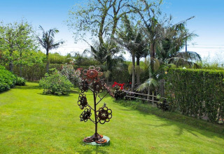 Groene tuin met palmbomen, struiken en een metalen bloemsculptuur bij Quinta dos Curubás in Portugal.