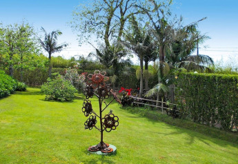 Giardino verde con palme, arbusti e scultura floreale in metallo alle Holiday homes Quinta dos Curubás in Portogallo.