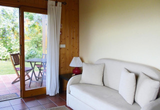 Lichte bungalow woonkamer met bank, kussens, lamp en schuifdeur naar terras met tuinmeubels in Portugal.