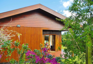 Knusse houten bungalow met terras omringd door bloemen en groen bij Quinta dos Curubás in Portugal.