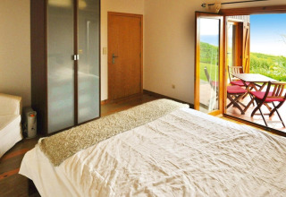 Slaapkamer in Holiday homes Quinta dos Curubás, Portugal, met bed, kast en uitzicht op terras met stoelen buiten.