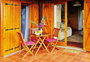 Patio in legno con tavolo e sedie davanti a bungalow di Quinta dos Curubás a Vila Franca do Campo, Portogallo.