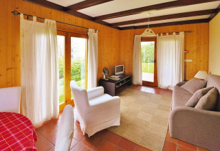 Lichte woonkamer in een vakantiehuis met houten wanden, grote ramen en knusse inrichting in Portugal.