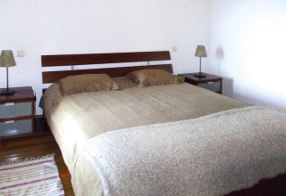 Slaapkamer met groot bed en twee nachtkastjes met lampen in een vakantiehuisje in Portugal.