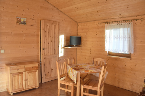Indretning i træ i hytte ved havet i Danmark med spisebord, stole, lille TV og vindue med gardin.