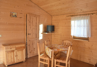 Gemütlicher Innenraum eines Holzhauses am Meer in Dänemark mit Esstisch, Stühlen und kleinem Fernseher.