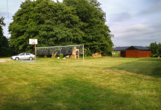 Sportplatz bei Cottages Ranch by the Sea in Dänemark mit Basketballkorb, Volleyballnetz und grünem Rasen.
