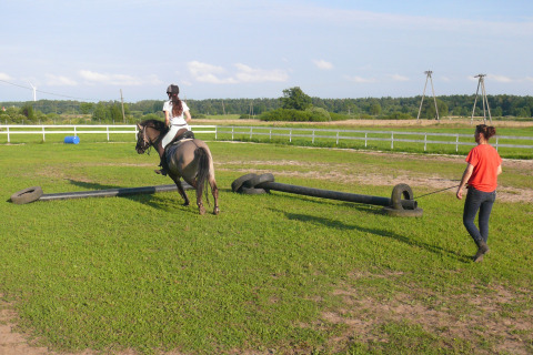 Una ragazza cavalca un cavallo con una allenatrice vicina in un prato a Cottages ranch by the sea in Danimarca.