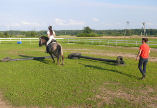 En pige rider på en hest med en træner ved siden af på en græsmark ved Cottages ranch by the sea i Danmark.