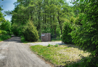 Grindweg naar het hek van 'Cottages ranch by the sea' omgeven door groen bos in Denemarken.