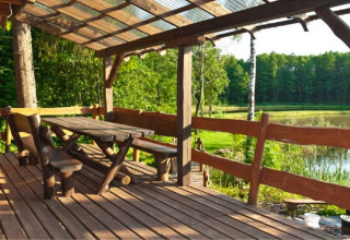 Terrasse en bois avec bancs, table et toit, vue sur le lac et la forêt à House Gajewo à Podlasie, Suède.