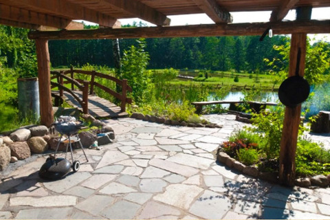 Terrasse en pierre avec barbecue, banc, jardin, pont et étang dans la verdure à House Gajewo.