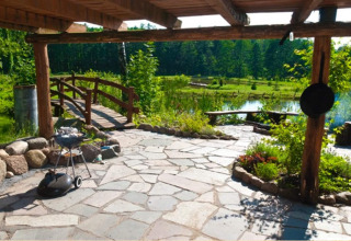 Terrasse en pierre avec barbecue, banc, jardin, pont et étang dans la verdure à House Gajewo.