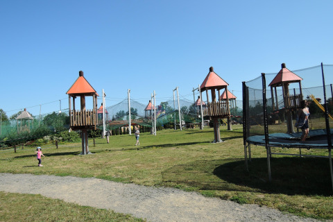 Kinderen spelen op een grasveld met torens, netten en trampoline bij een glampingaccommodatie buiten.