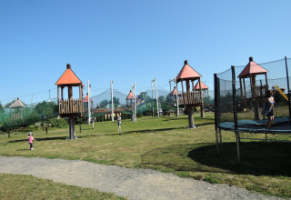 Kinderen spelen op een grasveld met torens, netten en trampoline bij een glampingaccommodatie buiten.