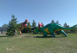 Twee grote dinosaurussen in het gras met bomen op de achtergrond en een kind dat voorbij rent.