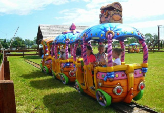 Kinderen maken een ritje in een kleurrijke minitrein bij een glampingverblijf met groen gras en hekjes.