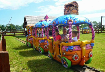 Kinderen op een kleurrijk minitreintje bij een glampingverblijf, omringd door gras en houten hekjes.