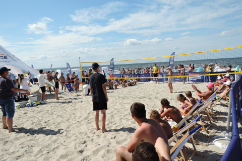 Mensen kijken naar een strandvolleybalwedstrijd bij zee op een glampinglocatie, zittend op ligstoelen.