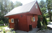 Gemütliches rotes Ferienhaus mit Satteldach, umgeben von Bäumen im Erholungsort Wiselka, Deutschland.