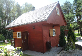Red wooden lodge with white windows and a steep roof, nestled among trees at a holiday resort in Wiselka.