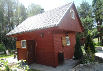 Rode houten vakantiewoning met witte ramen en hellend dak, omgeven door groen in Wiselka.