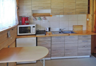 Compact kitchen with wood cabinets, table, microwave and coffee maker in Wiselka holiday resort, Germany.