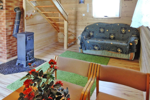 Cozy lodge interior with wood walls, a stove, sofa, green rugs, flowers on table, and wooden staircase.