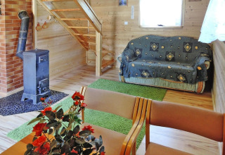 Hyggelig opholdsstue med trævægge, komfur, sofa, grønne tæpper, bord med blomster og en trappe op.