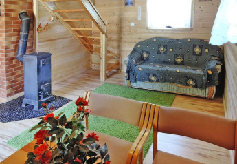 Knusse woonkamer van vakantieverblijf met houten muren, houtkachel, zetel, groene tapijten en trap.