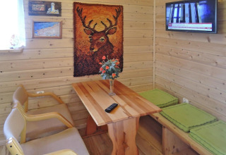 Gemütlicher Wohnbereich im Ferienhaus mit Holzvertäfelung, Hirschbild, TV, Tisch und Sitzgelegenheiten.
