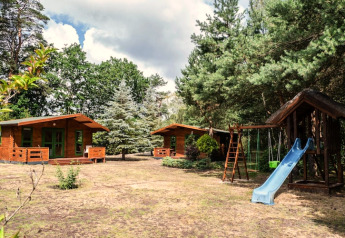 Deux chalets en bois et une aire de jeux avec toboggan et balançoires entourés d’arbres en Allemagne.