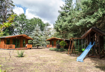 Dos casas de madera y un parque infantil con tobogán y columpios entre árboles en Kodrabek, Alemania.