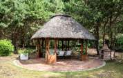 Kiosque de jardin rond avec toit de chaume et espace barbecue en forêt à Kodrabek, Allemagne.