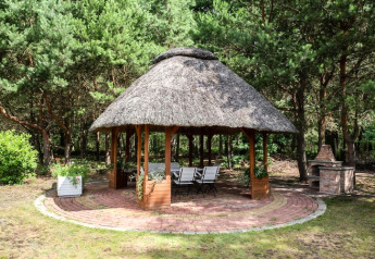 Runder Gartenpavillon mit Strohdach, Sitzplätzen und Grill im Grünen, Kodrabek, Deutschland.
