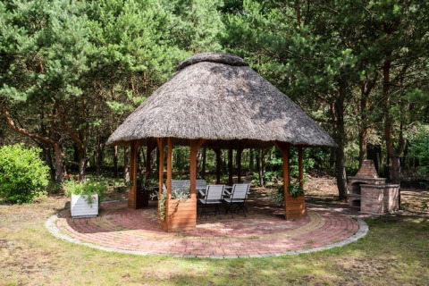 Runder Gartenpavillon mit Strohdach, Sitzplätzen und Grill im Grünen, Kodrabek, Deutschland.
