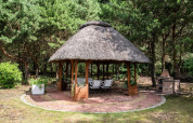 Runder Gartenpavillon mit Strohdach, Sitzplätzen und Grill im Grünen, Kodrabek, Deutschland.