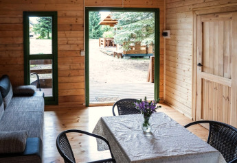 Innenraum eines Holzferienhauses mit Sofa, Esstisch und Blick durch offene Tür auf die Terrasse.