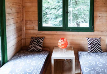 Deux lits simples dans un chalet en bois chaleureux en Allemagne, avec oreillers zèbre et lampe rouge.