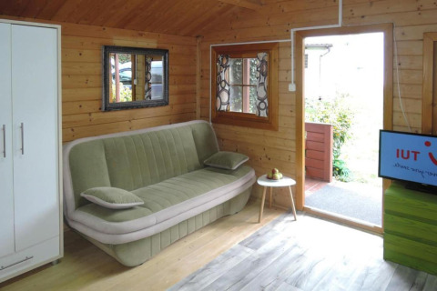 Living room of Bungalows Lubin Type A Jolanta in Germany, featuring green sofa, wood walls and TV.