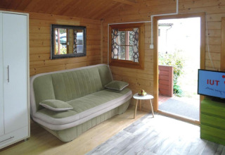 Living room of Bungalows Lubin Type A Jolanta in Germany, featuring green sofa, wood walls and TV.