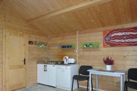 Vista interna di una baita in legno con angolo cottura, tavolo da pranzo, sedie e decorazione murale.