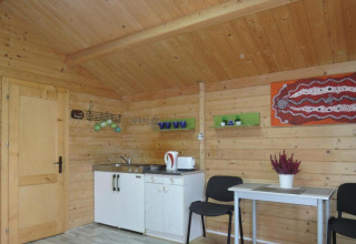 Vista interna di una baita in legno con angolo cottura, tavolo da pranzo, sedie e decorazione murale.