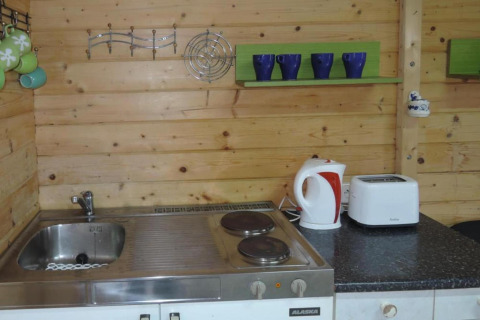 Piccola cucina in legno con lavello, fornelli, bollitore, tostapane e tazze colorate sulle mensole.