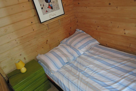 Cozy wooden cabin bedroom with striped bed, green nightstand, yellow lamp, and abstract wall art.