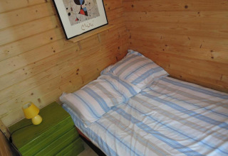 Cozy wooden cabin bedroom with striped bed, green nightstand, yellow lamp, and abstract wall art.