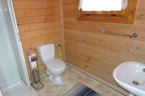 Bathroom in a wooden cabin with toilet, sink, shower, window, towel rails, and wooden walls.