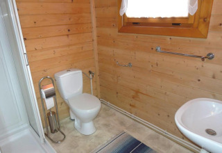 Bathroom in a wooden cabin with toilet, sink, shower, window, towel rails, and wooden walls.